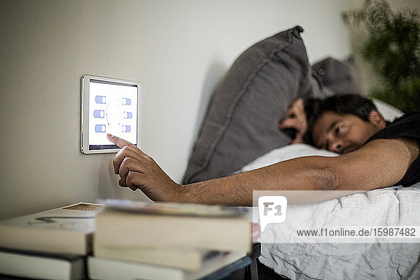 Mann benutzt digitales Tablett an der Wand  während er im Bett liegt  im Smart Home