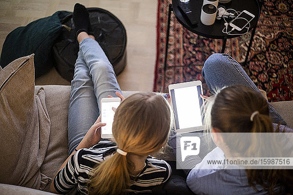 High angle view of sisters using wireless technologies while sitting on sofa at home