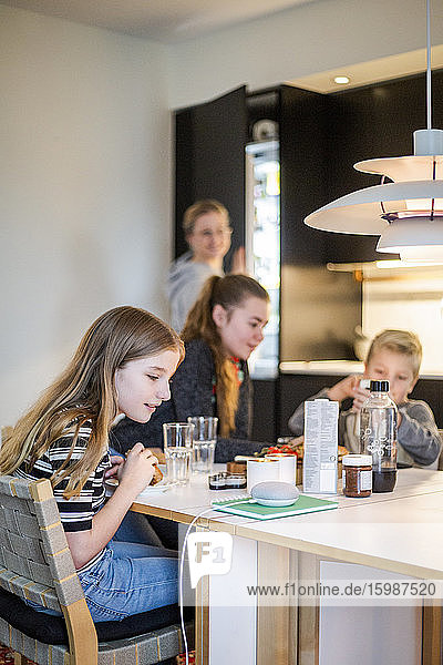 Mädchen unterhält sich mit kluger Rednerin  während sie mit der Familie am Tisch in einem modernen Haus sitzt