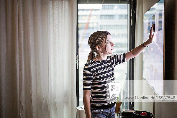 Mädchenberührende digitale Anzeige eines Fernsehgerätes im modernen Haus