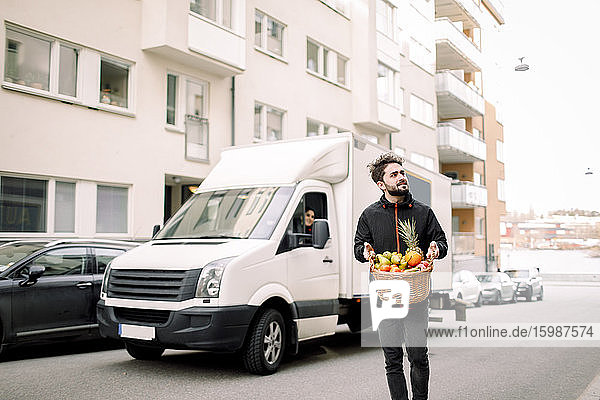 Junger Lieferwagenfahrer mit Obstkorb auf der Straße in der Stadt