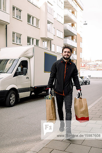Confident young delivery man carrying grocery bags on street in city