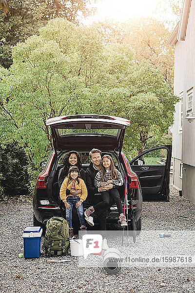 Lächelnde Eltern sitzen mit ihren Töchtern im Kofferraum eines Elektroautos
