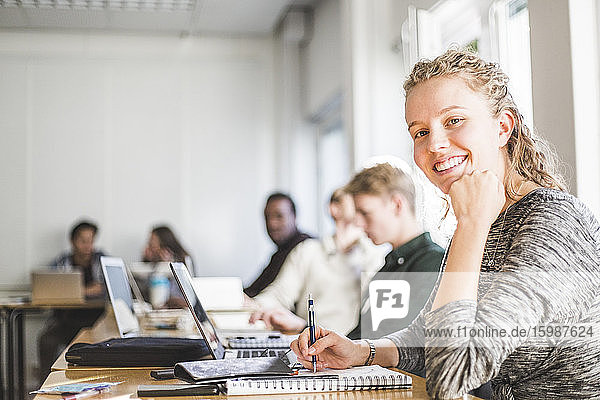 Porträt einer lächelnden jungen Frau am Schreibtisch im Klassenzimmer