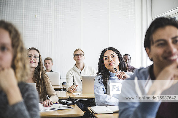 Multi-ethnische männliche und weibliche Studierende  die im Klassenzimmer am Schreibtisch sitzen