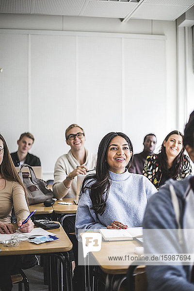 Multi-ethnische lächelnde männliche und weibliche Studenten sitzen am Schreibtisch im Klassenzimmer
