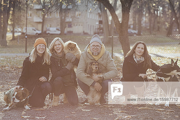 Porträt eines glücklichen Mannes und einer glücklichen Frau  die im Herbst mit Hunden im Park kauern