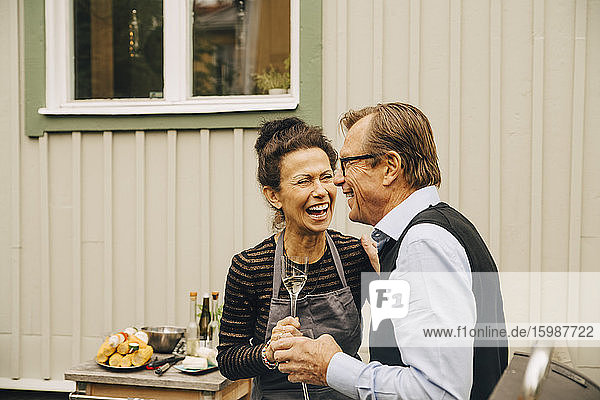 Älterer Mann und Frau lachen  während sie während einer Party im Hinterhof ein Getränk in der Hand halten
