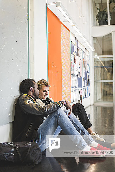 Junger Mann sitzt mit männlichem Freund auf dem Flur der Universität