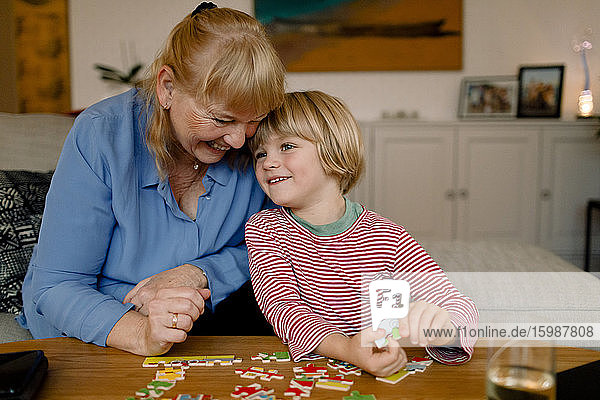 Lächelnder Enkel und Großmutter spielen zu Hause mit dem Puzzle