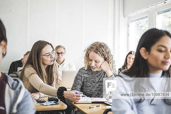 Female students discussing over book at desk in classroom