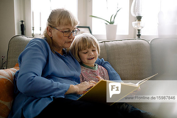 Großmutter liest Märchenbuch für Enkel  während sie auf dem Sofa im Wohnzimmer sitzt