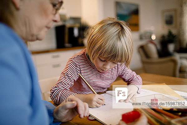 Junge macht bei Tisch Hausaufgaben bei der Großmutter