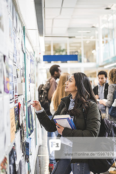 Young female student reading posters in university