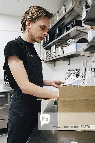 Seitenansicht der Bestandsliste junger androgyner Barista in einem Pappkarton in der Café-Küche