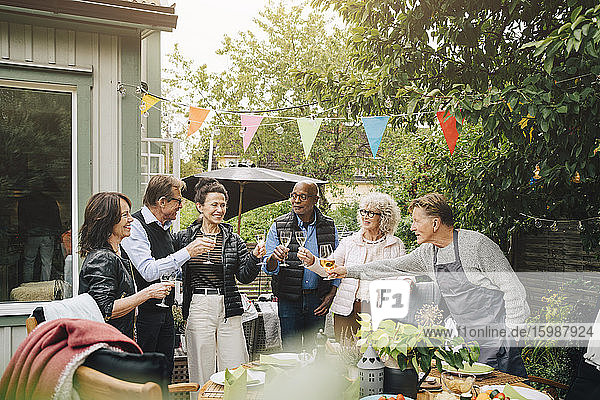 Aktive männliche und weibliche Seniorenfreunde stoßen mit einem Getränk an  während sie während eines Gartenfestes im Hinterhof stehen