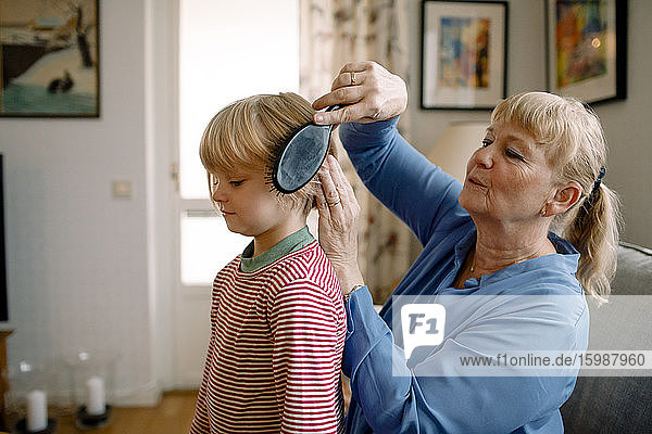 Seitenansicht einer älteren Frau  die zu Hause im Wohnzimmer die Haare ihres Enkels kämmt