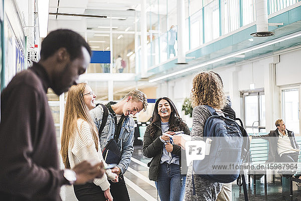 Fröhliche junge Studentinnen und Studenten unterhalten sich im Stehen in der Cafeteria der Universität