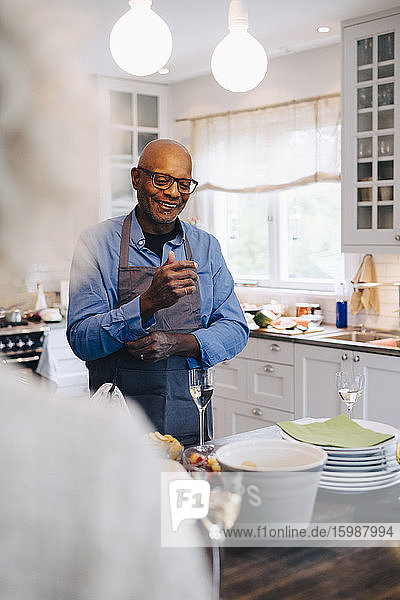 Lächelnder kahlköpfiger älterer Mann krempelt die Ärmel hoch  bevor er zu Hause in der Küche das Abendessen zubereitet