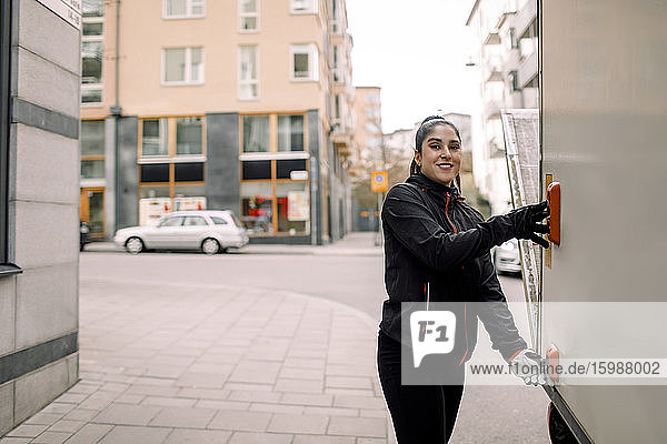 Portrait of confident young delivery woman with truck in city