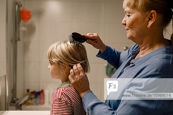 Side view senior woman combing hair of grandson in bathroom at home
