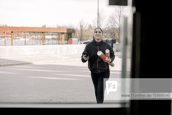 Lächelnde junge Zustellerin hält Pakete beim Gehen auf der Straße