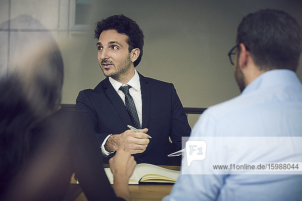 Junger männlicher Geschäftsmann sitzt mit Kollegen während eines Treffens in einer Anwaltskanzlei