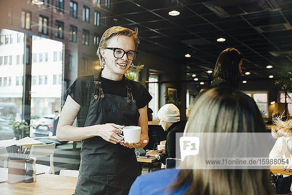 Lächelnder  junger  transsexueller Barista beim Gespräch mit einer Kundin in der Cafeteria