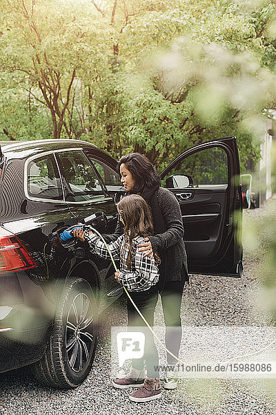 Mittlere erwachsene Frau  die ihrer Tochter beibringt  Elektroautos an der Ladestation aufzuladen
