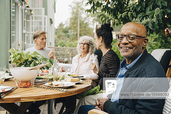 Porträt eines lächelnden kahlköpfigen älteren Mannes  der während der Dinnerparty mit Freunden am Esstisch sitzt
