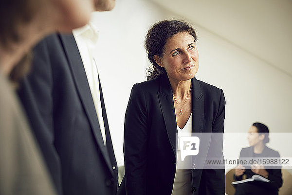 Confident businesswoman looking away while standing with lawyers at office during meeting