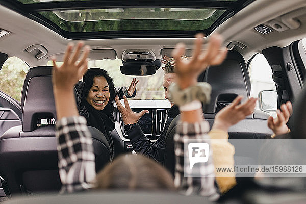 Fröhliche Familie reicht sich die Hand und genießt die Fahrt im Elektroauto