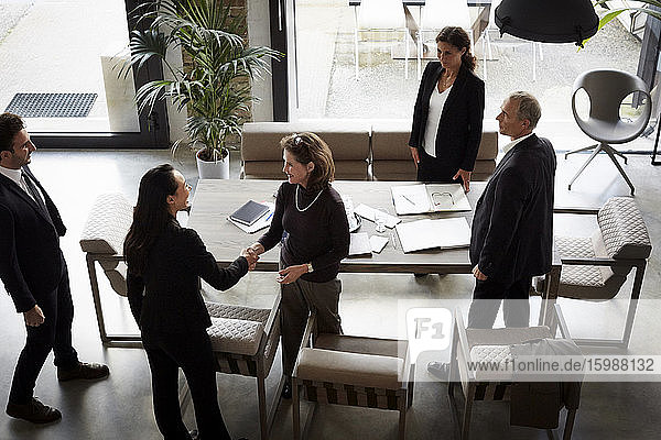 High angle view of female financial advisor greeting businesswoman while colleagues standing in office during meeting