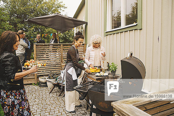 Lächelnde ältere Frauen beim Zubereiten des Abendessens auf dem Grill im Hinterhof