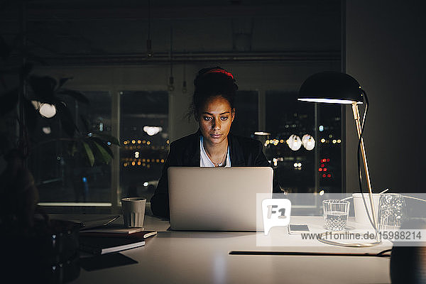 Engagierte junge Geschäftsfrau arbeitet bis spät in die Nacht  während sie den Laptop im Kreativbüro benutzt