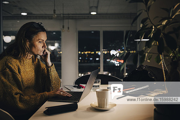 Seitenansicht einer engagierten reifen Geschäftsfrau  die einen Laptop benutzt  während sie spät im Kreativbüro arbeitet