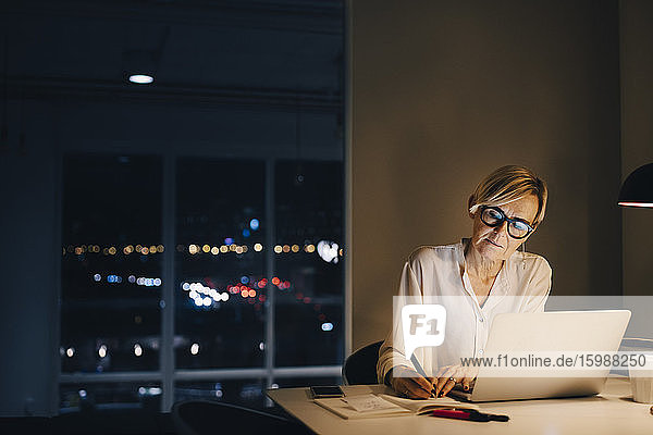 Selbstbewusste Unternehmerin schreibt im Buch  während sie mit dem Laptop am Bürotisch sitzt