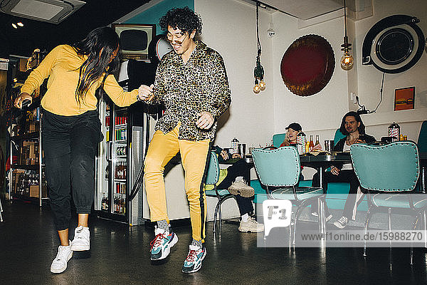 Lächelnder junger Mann und tanzende Frau  während Freunde im Hintergrund im Cafe zuschauen