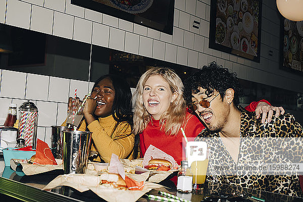 Porträt einer glücklichen Frau  die mit Freunden während eines geselligen Beisammenseins im Café Burger isst
