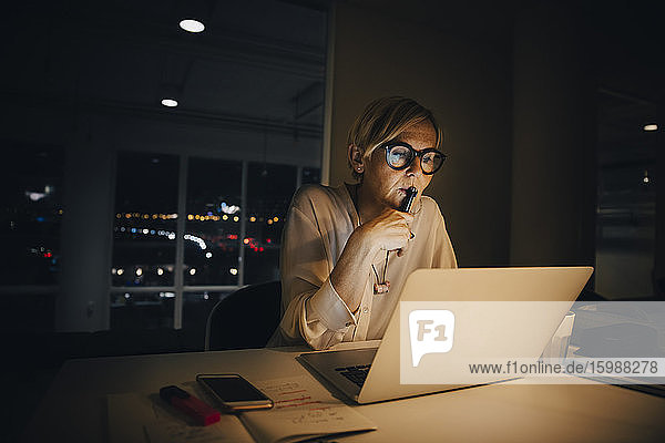 Nachdenkliche Geschäftsfrau schaut auf den Laptop  während sie spät im Kreativbüro arbeitet