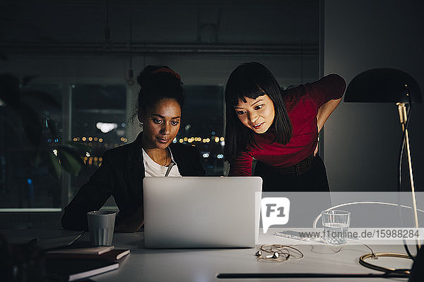 Zuversichtliche weibliche Geschäftskollegen diskutieren am Laptop  während sie spät im Kreativbüro arbeiten