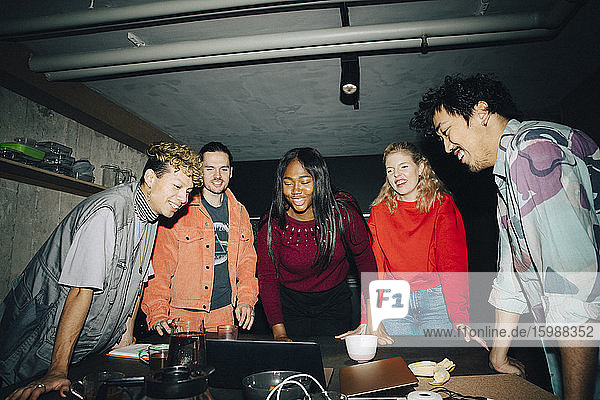 Lächelnde Unternehmer schauen auf den Laptop  während sie im Kreativbüro am Tisch stehen