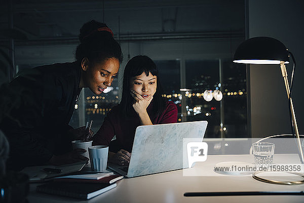 Selbstbewusste Geschäftsfrauen planen ihre Strategie  während sie bei nächtlichen Besprechungen im Büro den Laptop benutzen