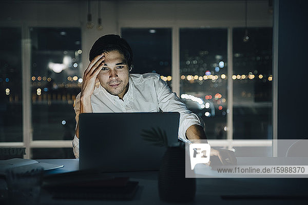 Businessman looking at laptop while working late in dark creative workplace