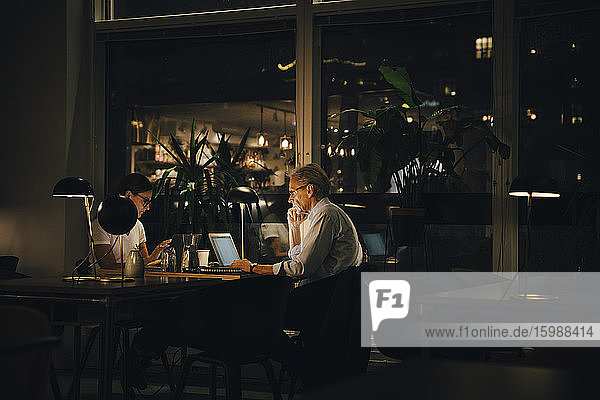 Male and female professionals working late in dark office at night
