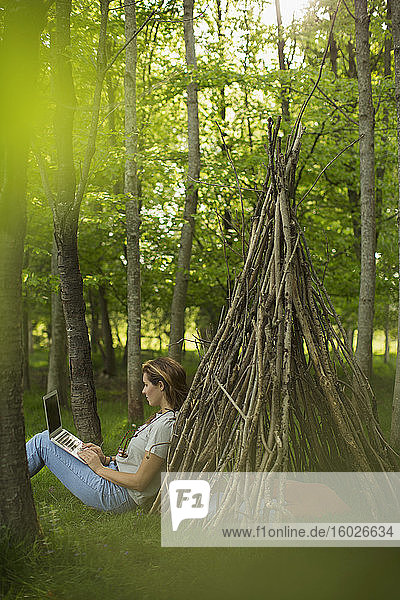 Frau mit Laptop am Ast-Tipi im Wald
