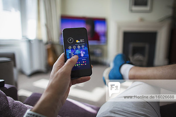 POV Mann regelt die Temperaturregelung am Smartphone im Wohnzimmer