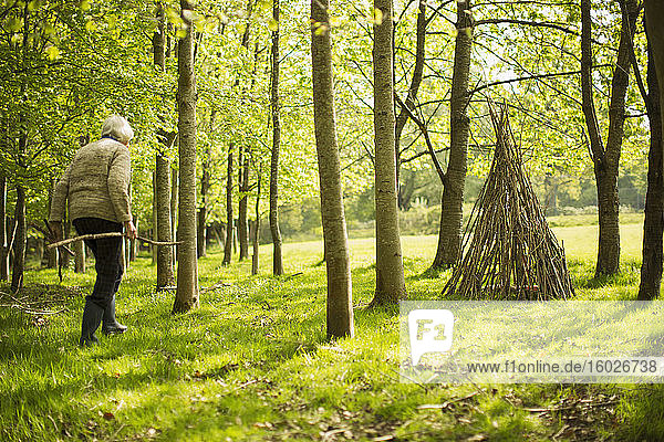 Ältere Frau mit Ästen beim Tipi-Basteln im sonnigen Wald