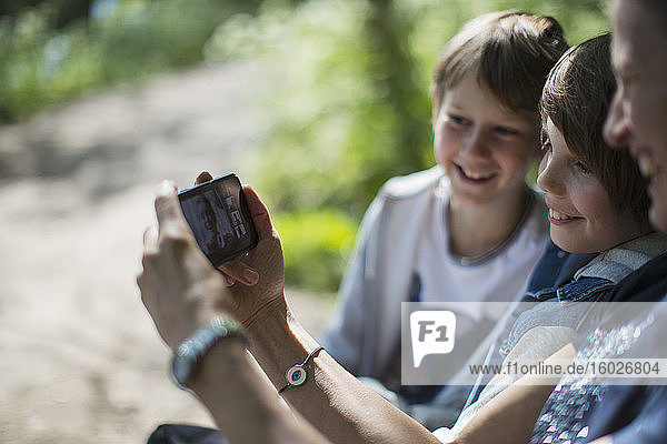Mother and sons video chatting with friends on smart phone in park