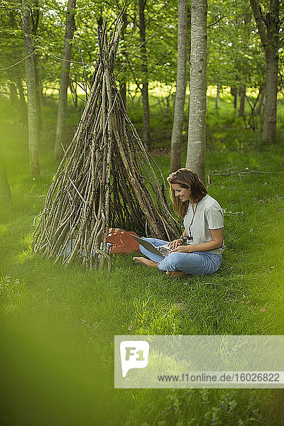 Frau mit Laptop entspannt sich am Ast-Tipi im Wald